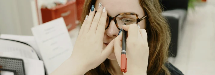 Close-up of a person wearing eyeglasses while another hand adjusts the frame using a small tool near the lens area.