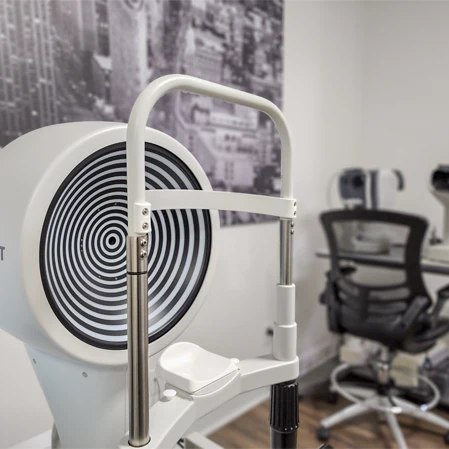 Eye exam device with concentric circle target, positioned near a chair and desk in a clinical room setting.