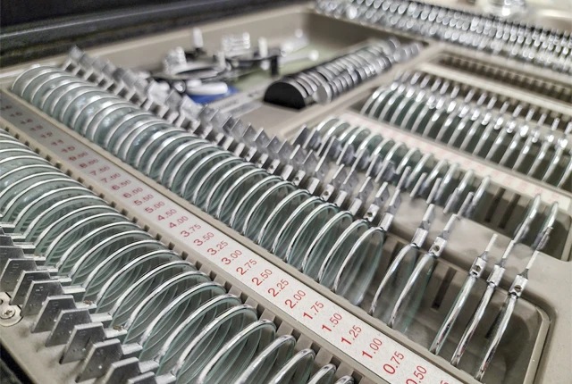 Tray of ophthalmic trial lenses arranged in rows with labeled measurements and metal frames inside a case.